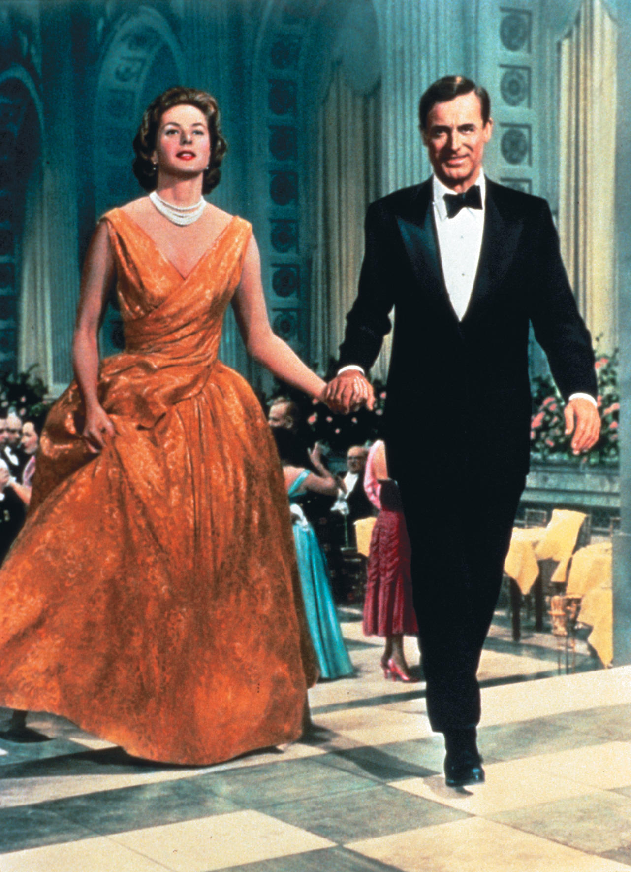 Ein Paar geht auf einer Tanzfläche, die Frau in einem orangefarbenen Kleid, der Mann im Smoking.