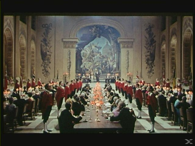 Szene aus einem Film, ein Bankettsaal mit Personen, die an einer langen Tafel sitzen.