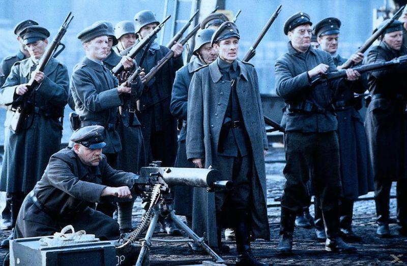 Soldaten mit Gewehren und einem Maschinengewehr, ein Offizier steht vorne, in einer Kriegsszene.