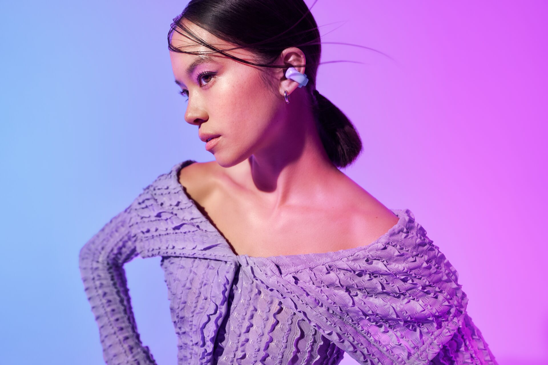 Kobieta z różowym i fioletowym oświetleniem. Ubrana w fioletową sukienkę, ze słuchawkami.