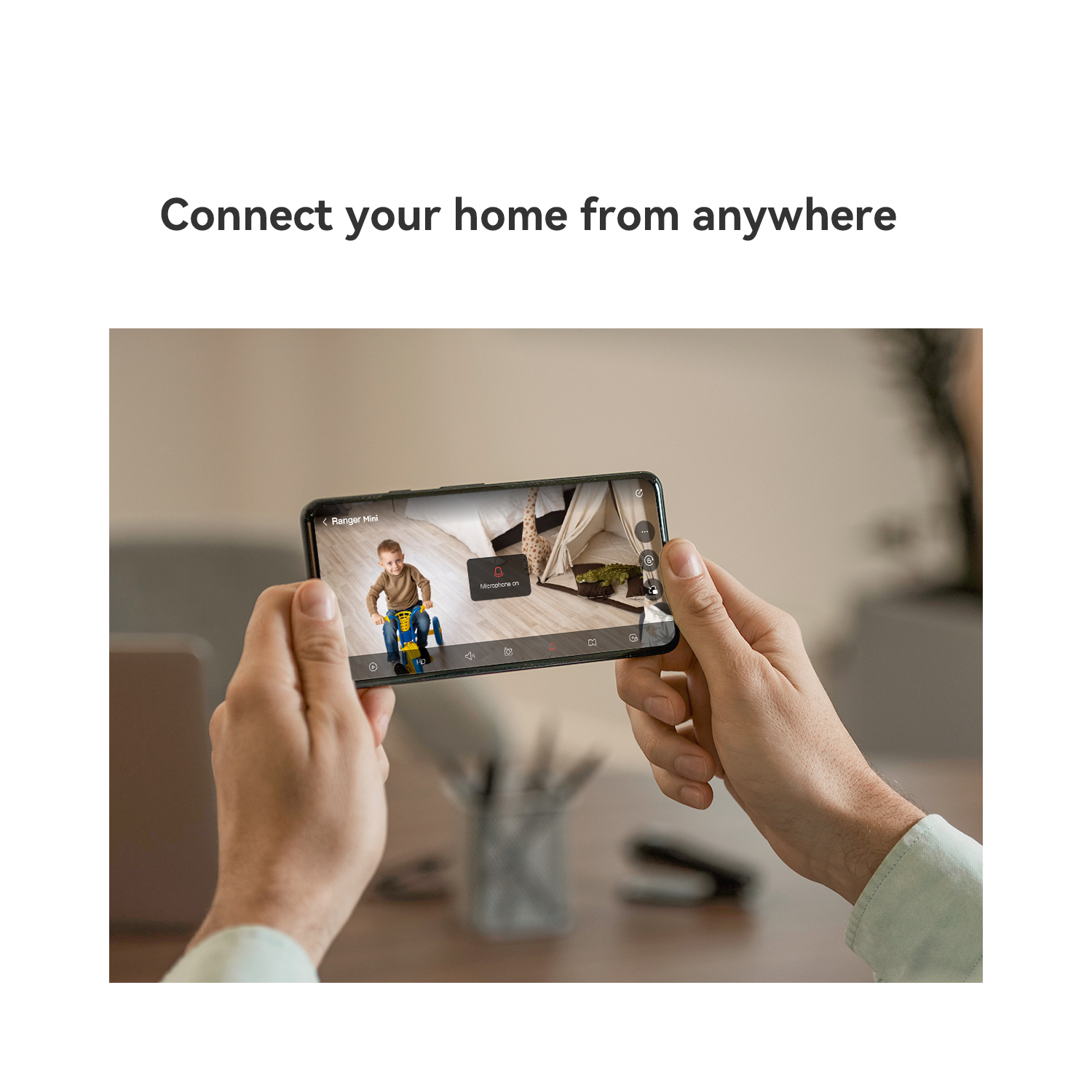 Person holding smartphone showing live video feed of a child on a toy vehicle.