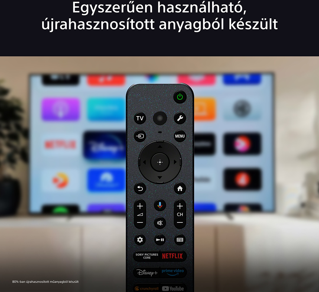 Fekete távirányító gombokkal, egy elmosódott TV-képernyő előtt, alkalmazásokkal.