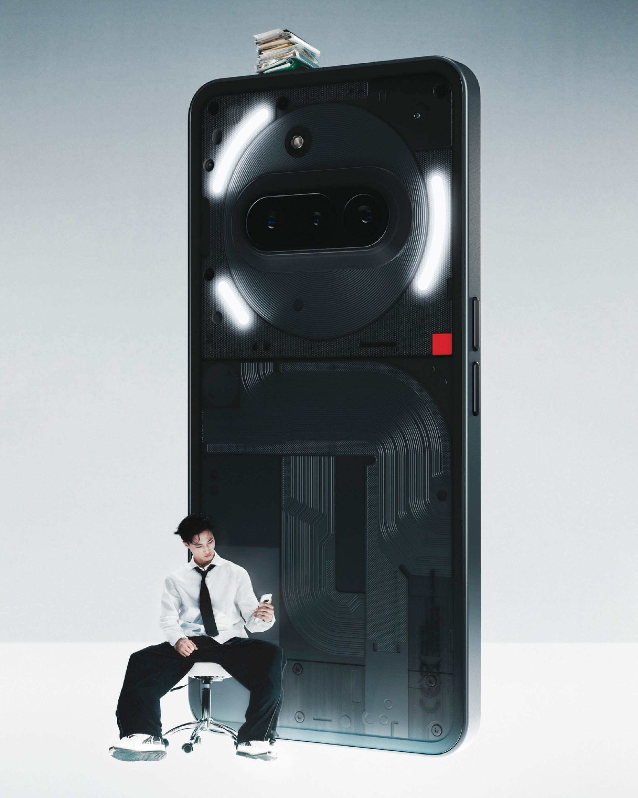 Une personne assise à côté d'un grand téléphone avec une pile de livres dessus. Le téléphone a un dos transparent.