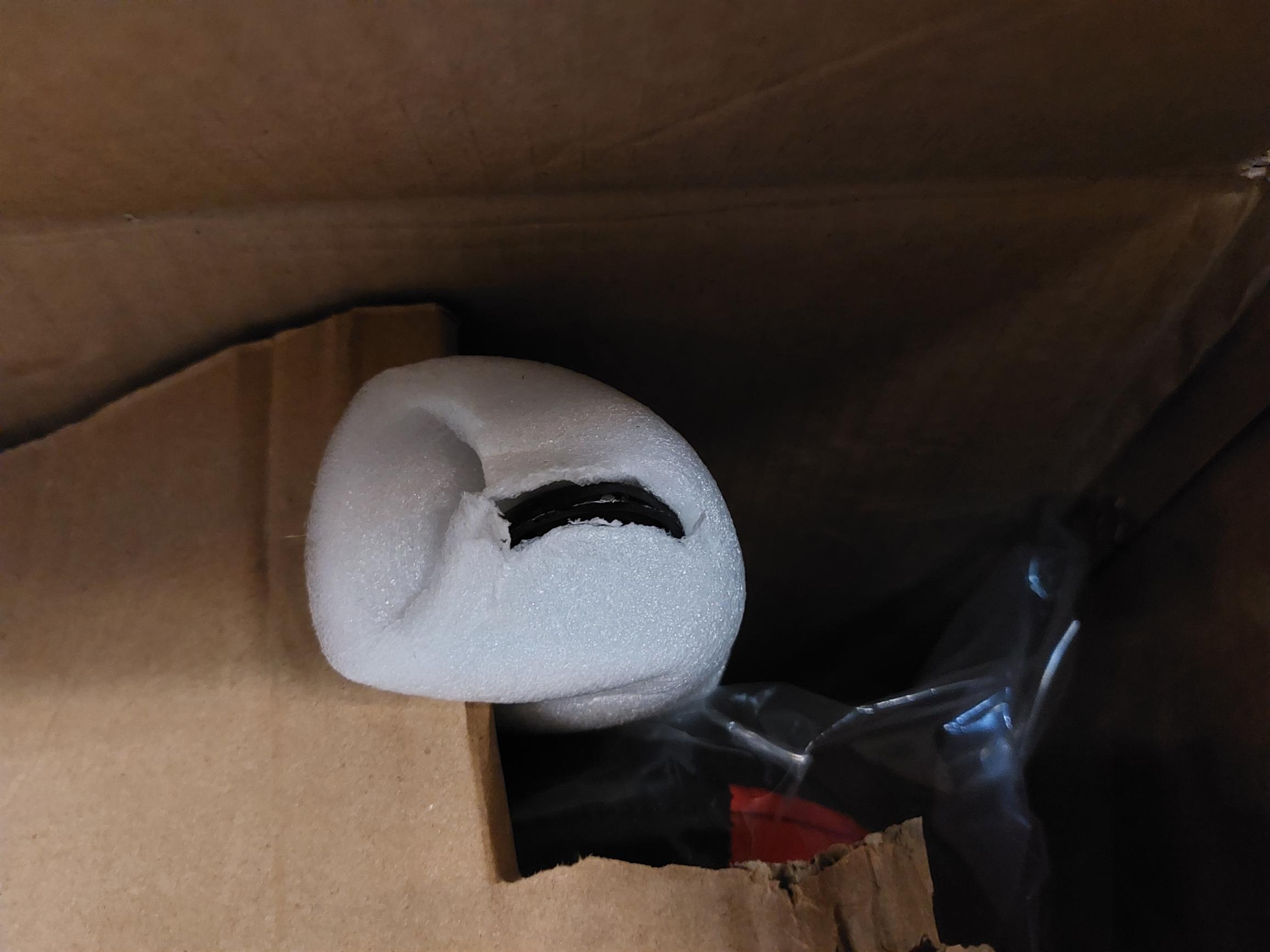 Biała pianka z czarnym przedmiotem w środku, w brązowym kartonowym pudełku.