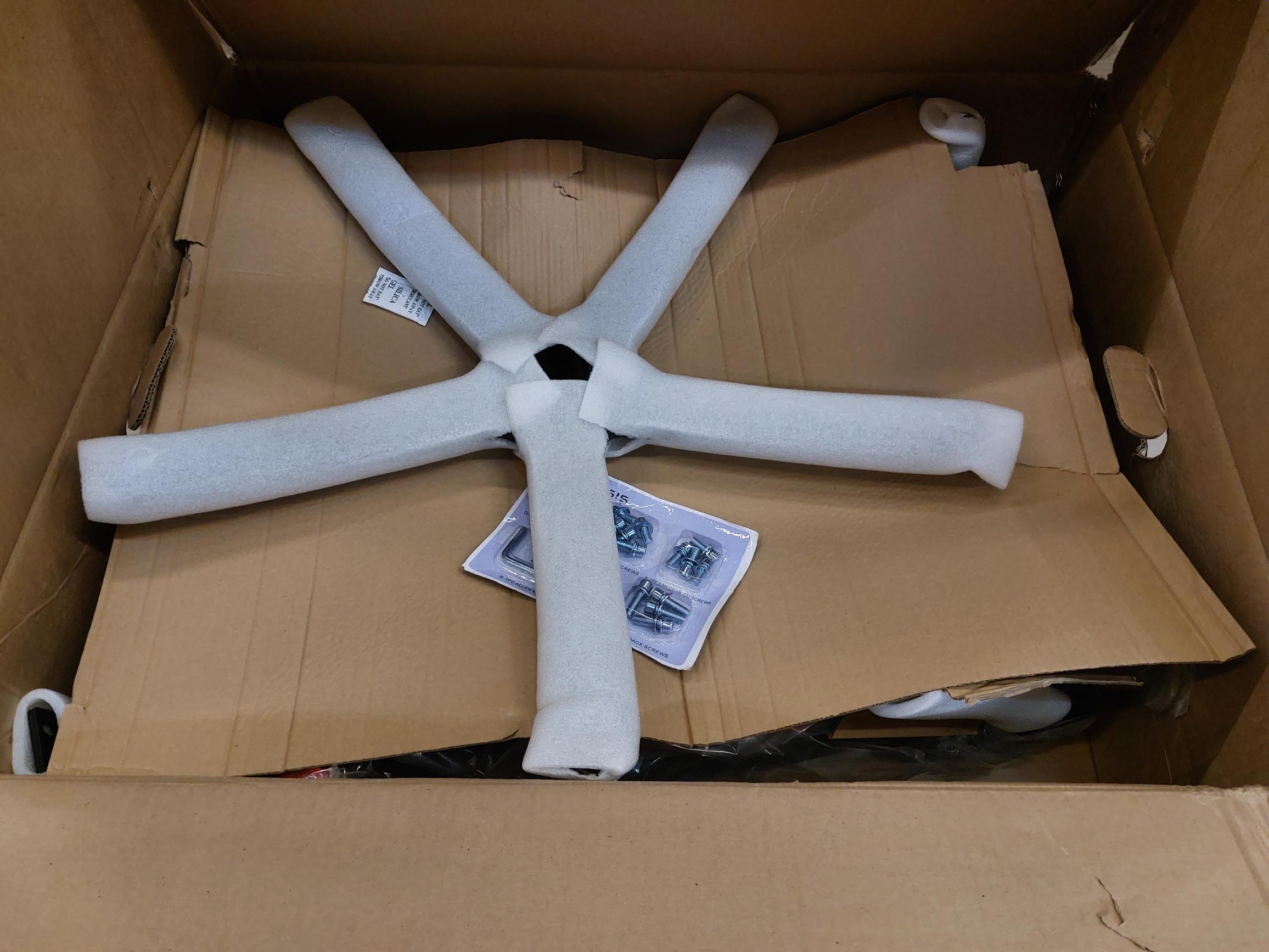 Zdemontowana podstawa krzesła wewnątrz kartonowego pudełka, elementy owinięte pianką ochronną.