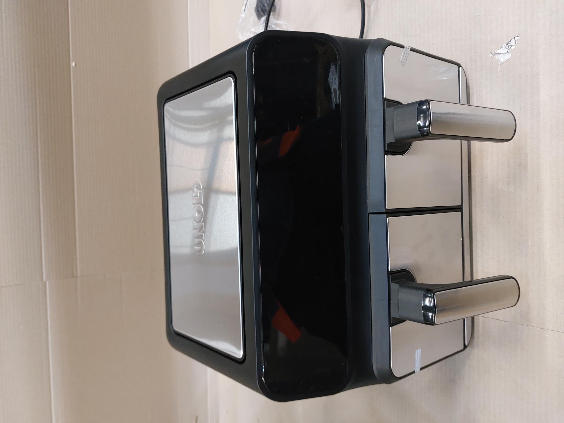 Czarna i srebrna frytkownica powietrzna z uchwytami, na beżowej powierzchni.