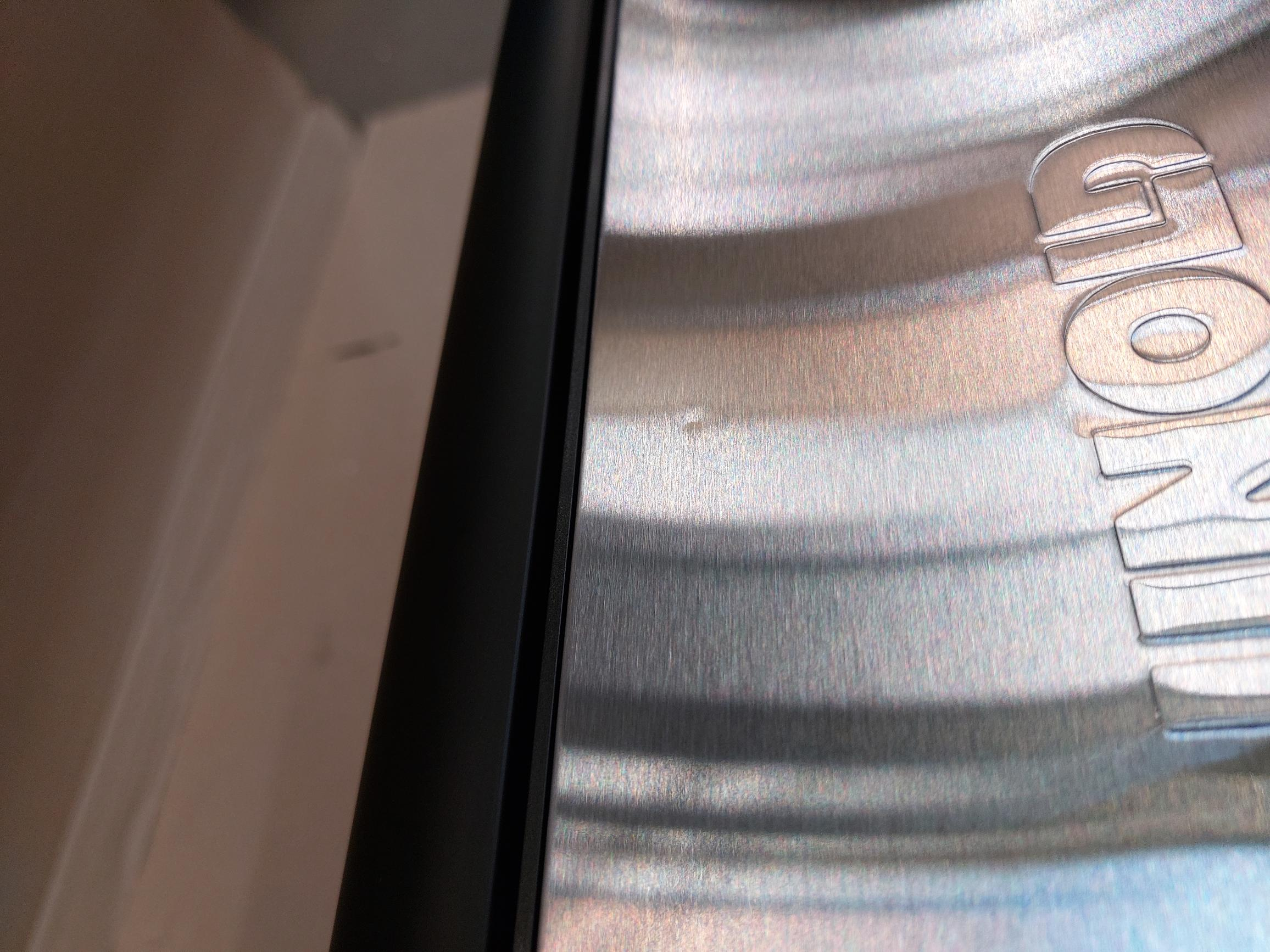 Zbliżenie powierzchni ze stali nierdzewnej z ciemnym wykończeniem, na powierzchni widoczny jest mały biały znak.