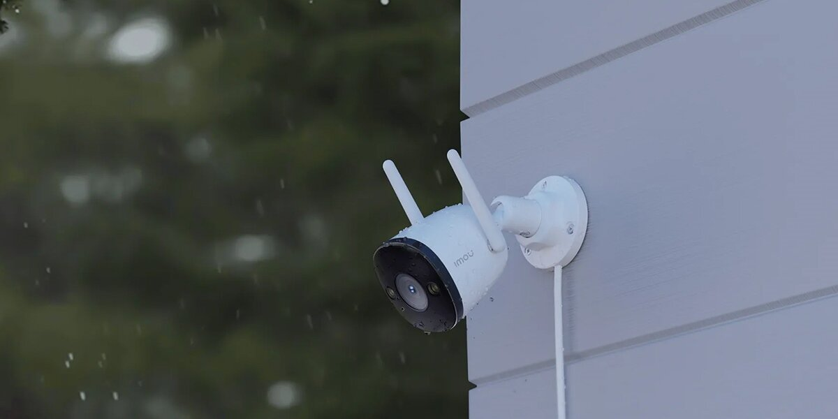 Biała zewnętrzna kamera bezpieczeństwa z dwiema antenami, zamontowana na ścianie.