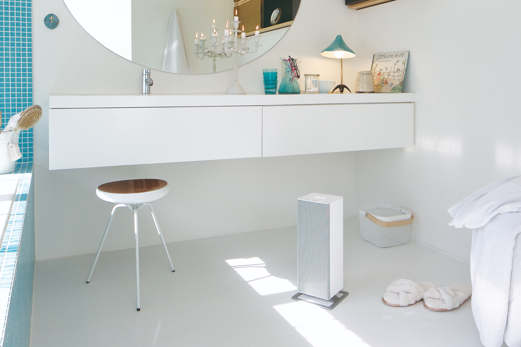 Une salle de bain avec un radiateur blanc, un miroir et des meubles blancs. Une serviette blanche à droite.
