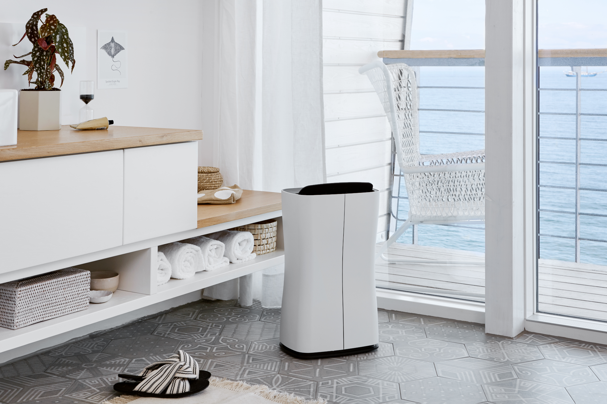 Una scena di bagno moderno con un purificatore d'aria bianco, mobili bianchi e vista sul mare.