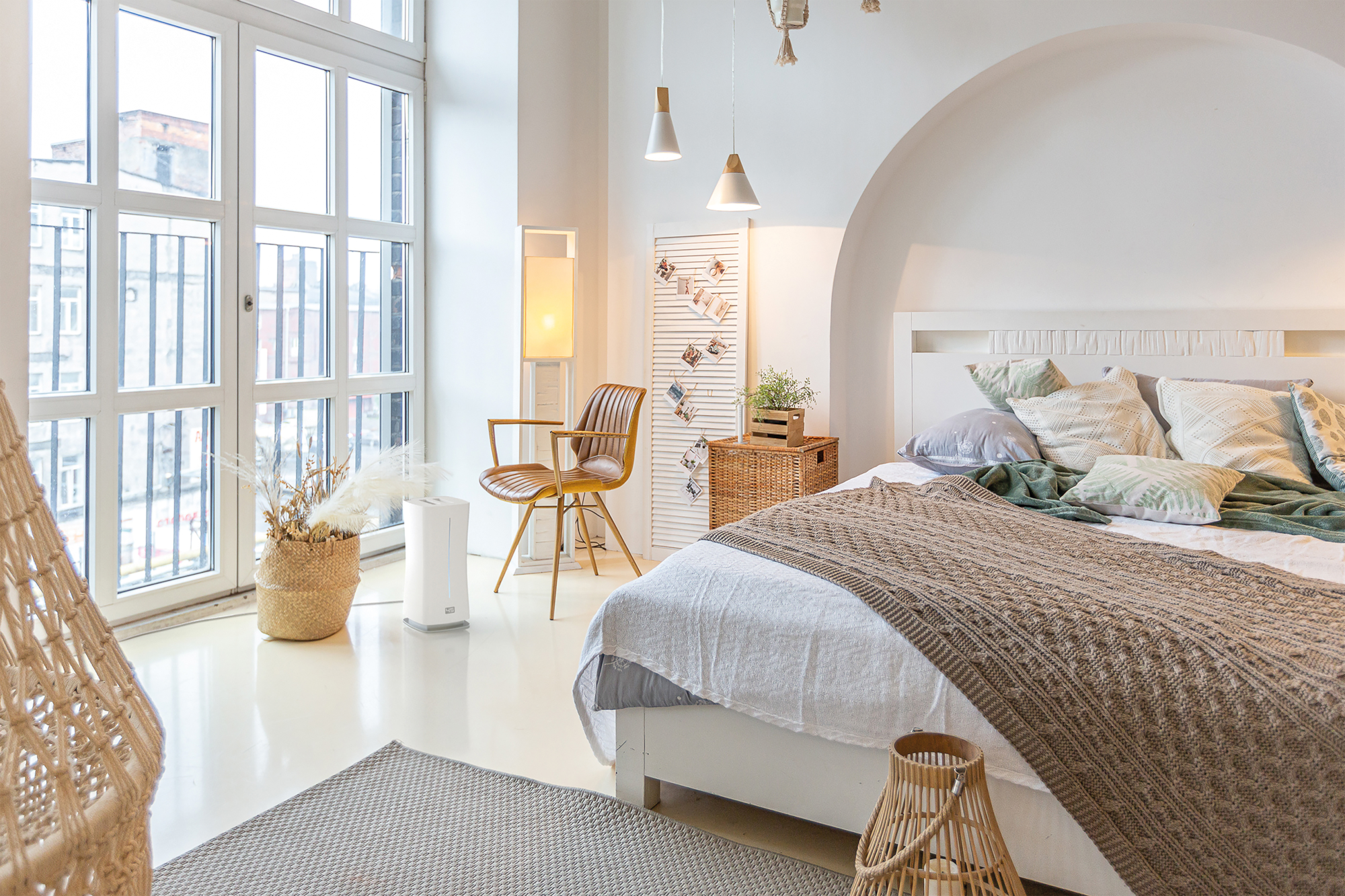 Helles, weißes Schlafzimmer mit großem Fenster, Bett, Stuhl und dekorativen Elementen. Tageslicht.