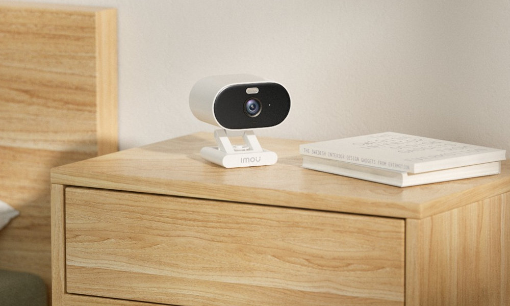 Biała kamera bezpieczeństwa na drewnianej szafce nocnej obok książek.