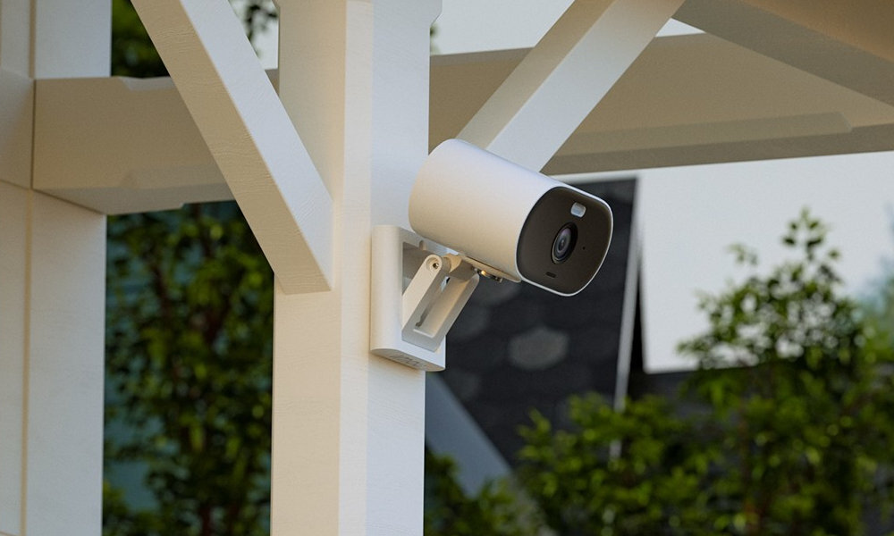 Biała kamera bezpieczeństwa zamontowana na białym drewnianym słupie. Zielone drzewa w tle.
