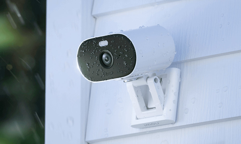 Biała zewnętrzna kamera bezpieczeństwa zamontowana na białej ścianie, widoczne krople deszczu.