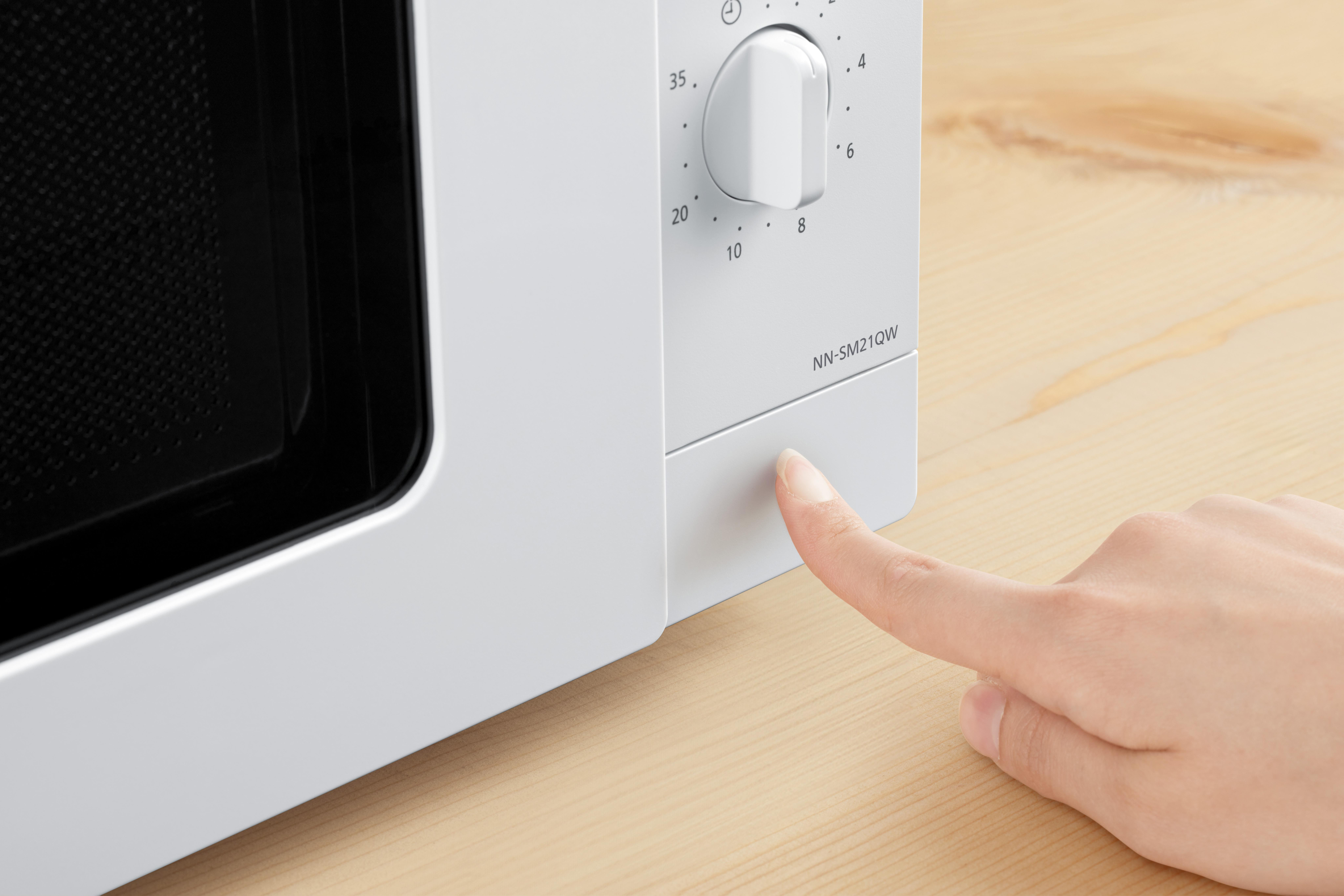 Der Finger einer Person drückt auf eine Taste einer weißen Mikrowelle, Nahaufnahme.