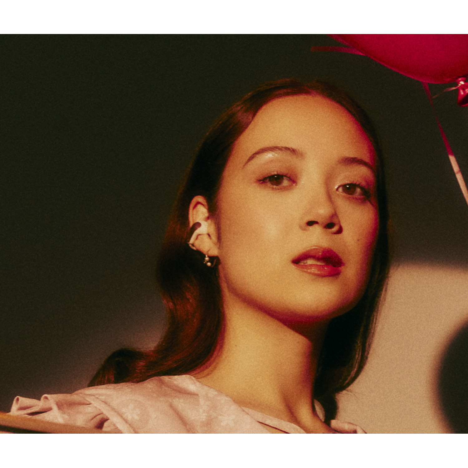 A woman with a pink shirt, earrings and red lipstick looks at the camera.