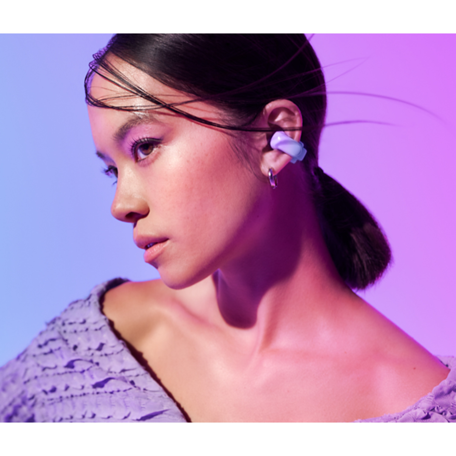 A woman with purple earbuds. She is looking left against a gradient blue and pink background.