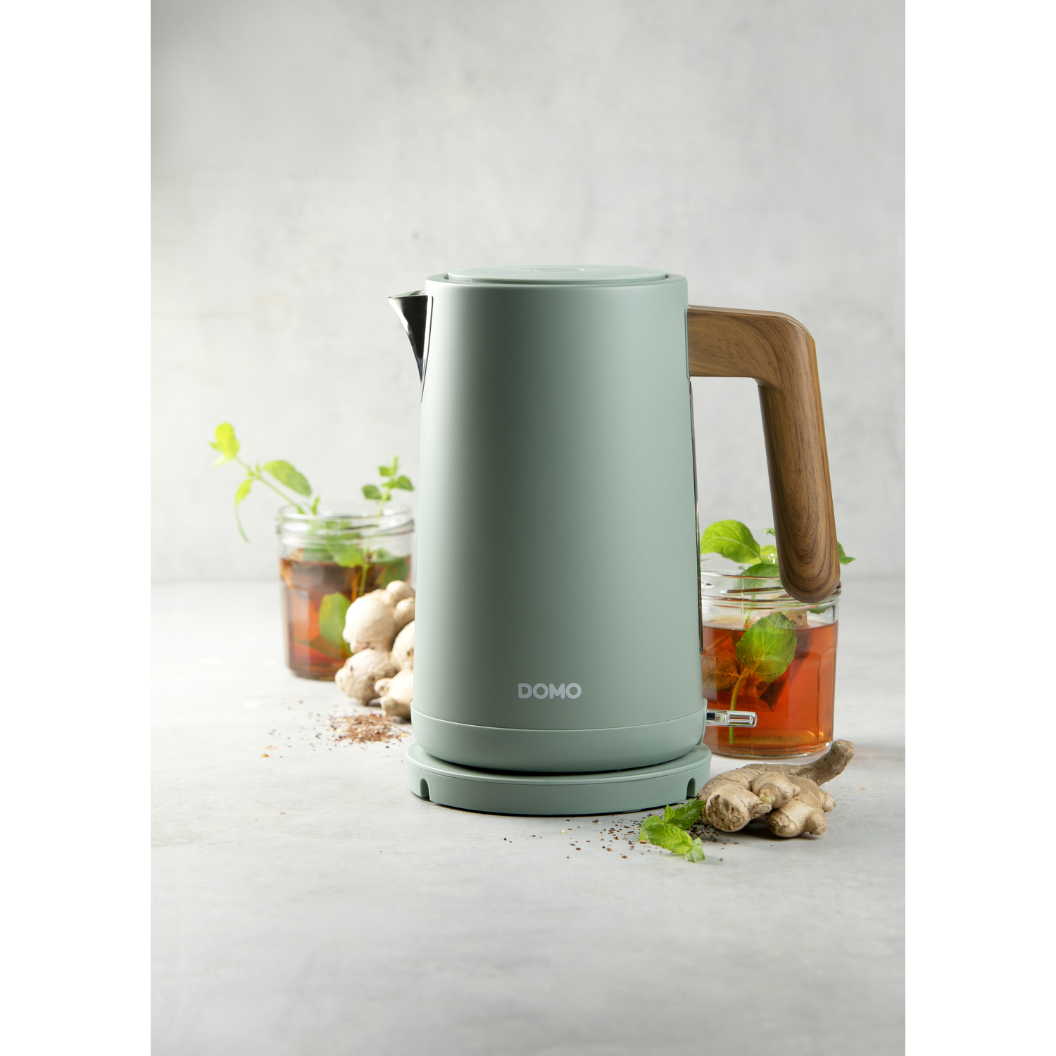 Een elektrische waterkoker met een lichtgroene behuizing en houten handvat, thee en gember.