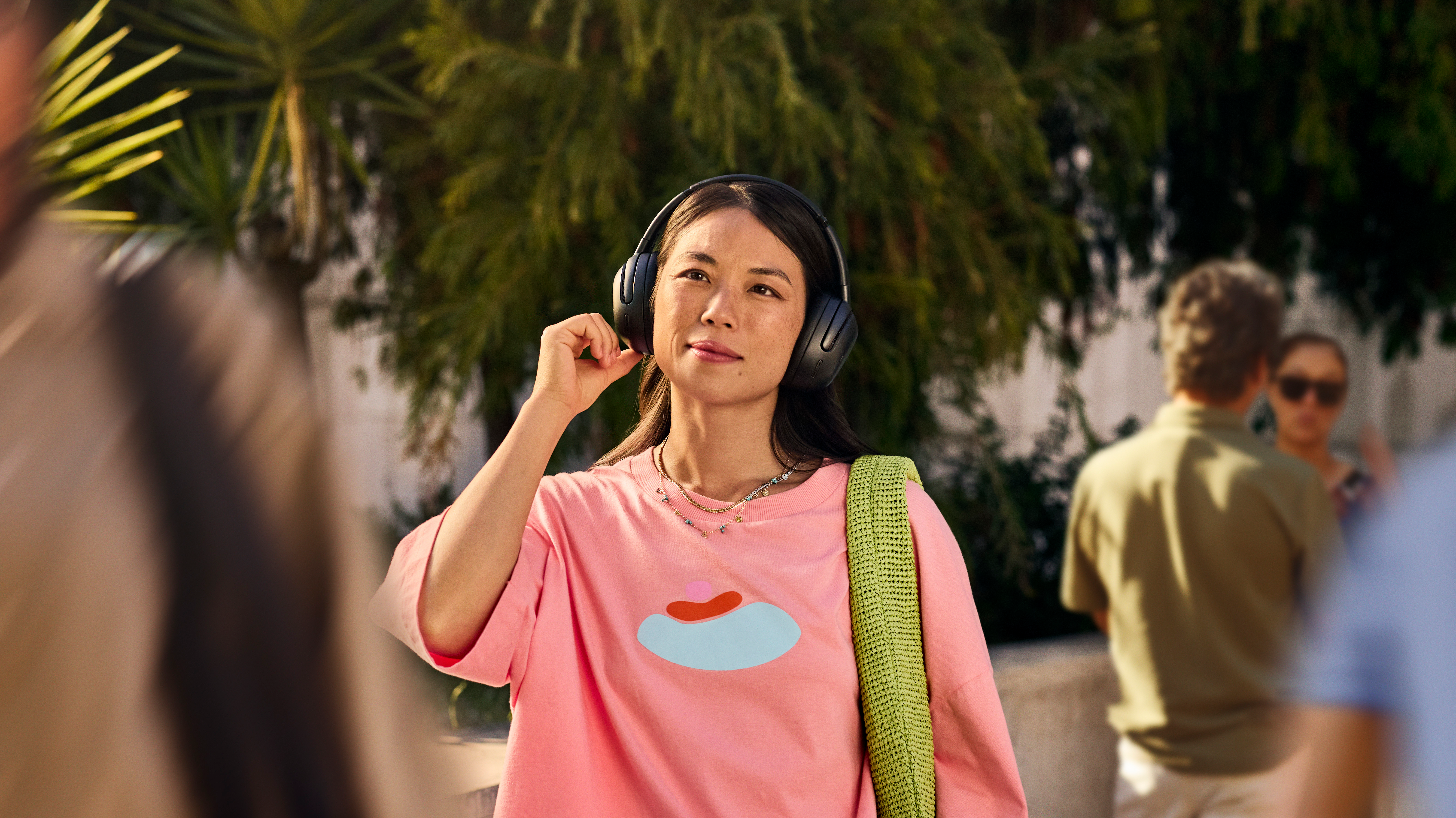 Donna con cuffie nere, camicia rosa, borsa verde, in piedi fuori.