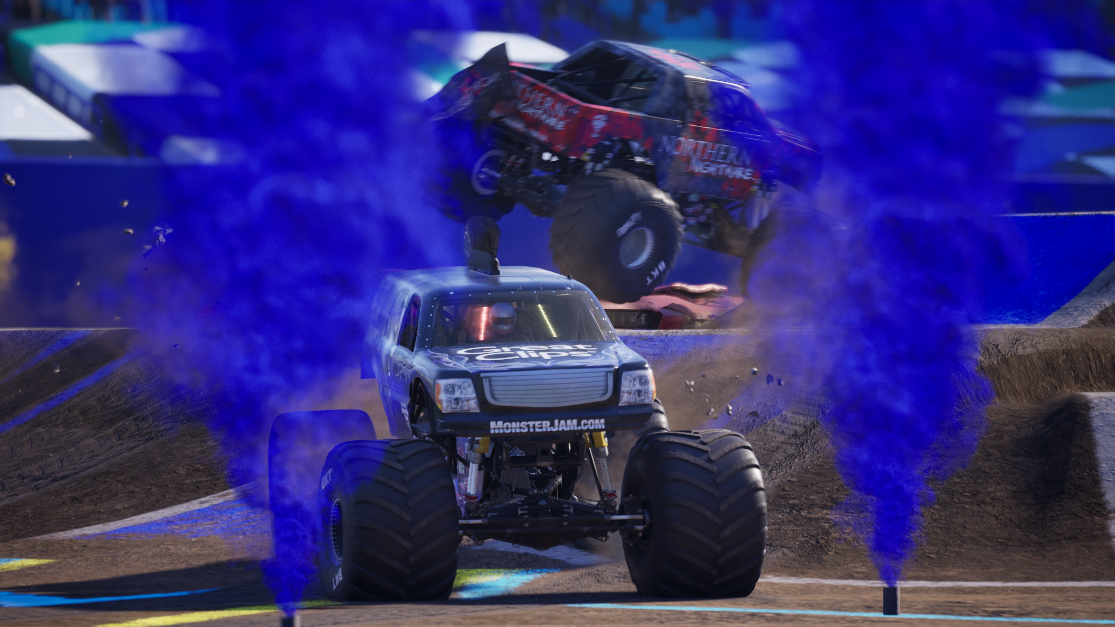 Due monster truck con fumo blu su una pista sterrata.