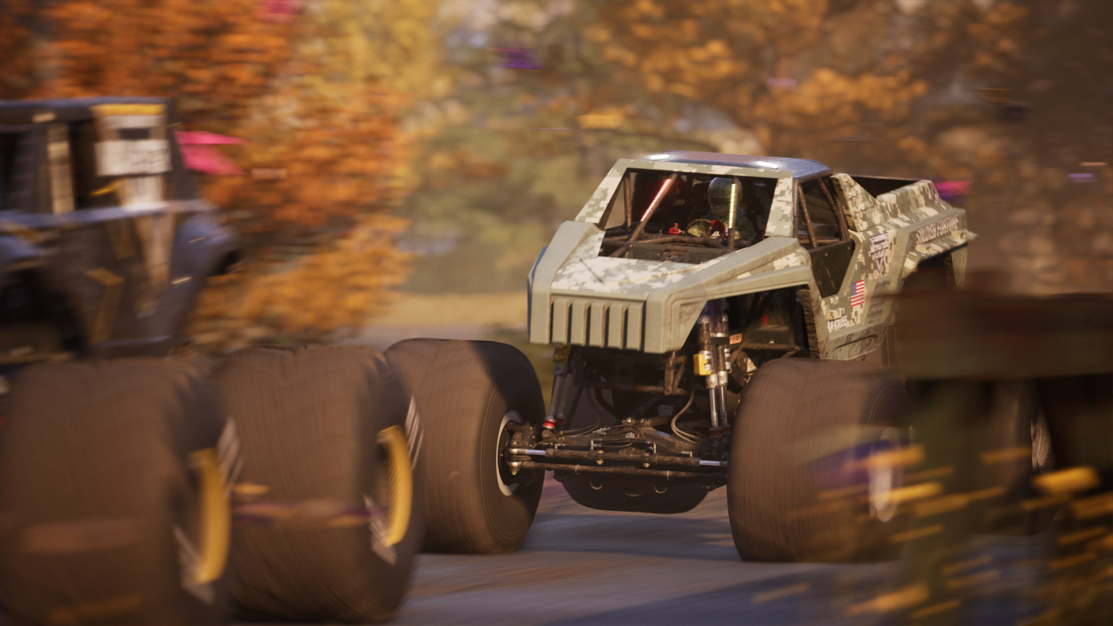Monster truck in movimento. Il camion è verde oliva e ha pneumatici grandi. Sfondo sfocato di alberi.
