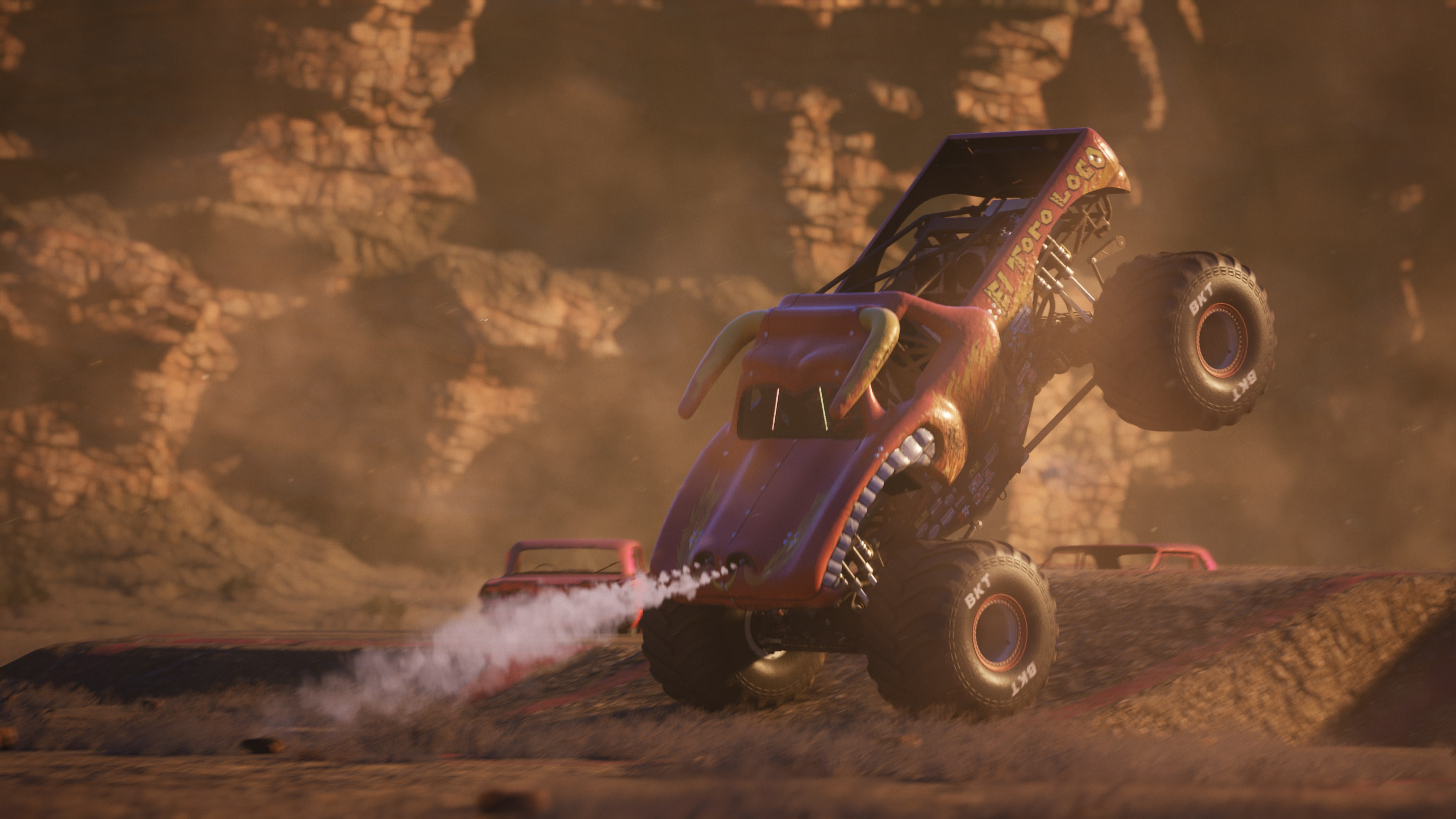 Un monster truck che fa un'impennata in una scena desertica, con un'auto rossa sullo sfondo.