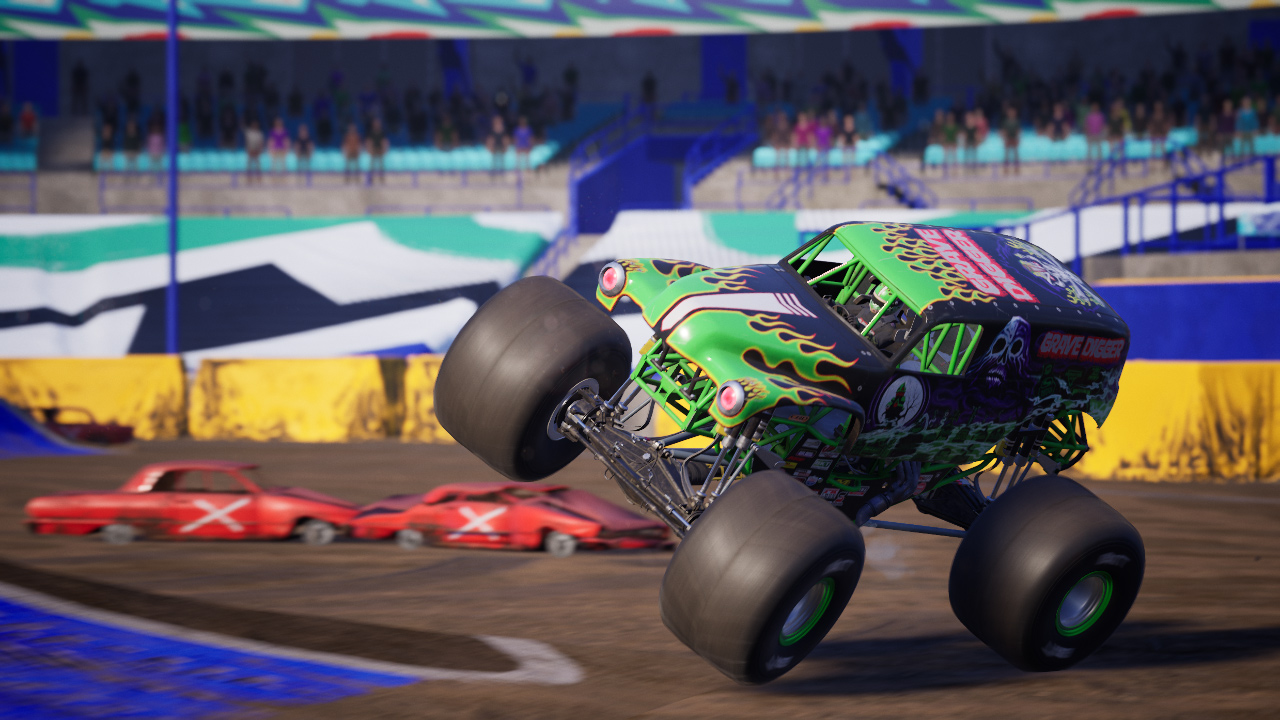 Un monster truck verde e nero che salta in uno stadio, con altri veicoli sfocati.