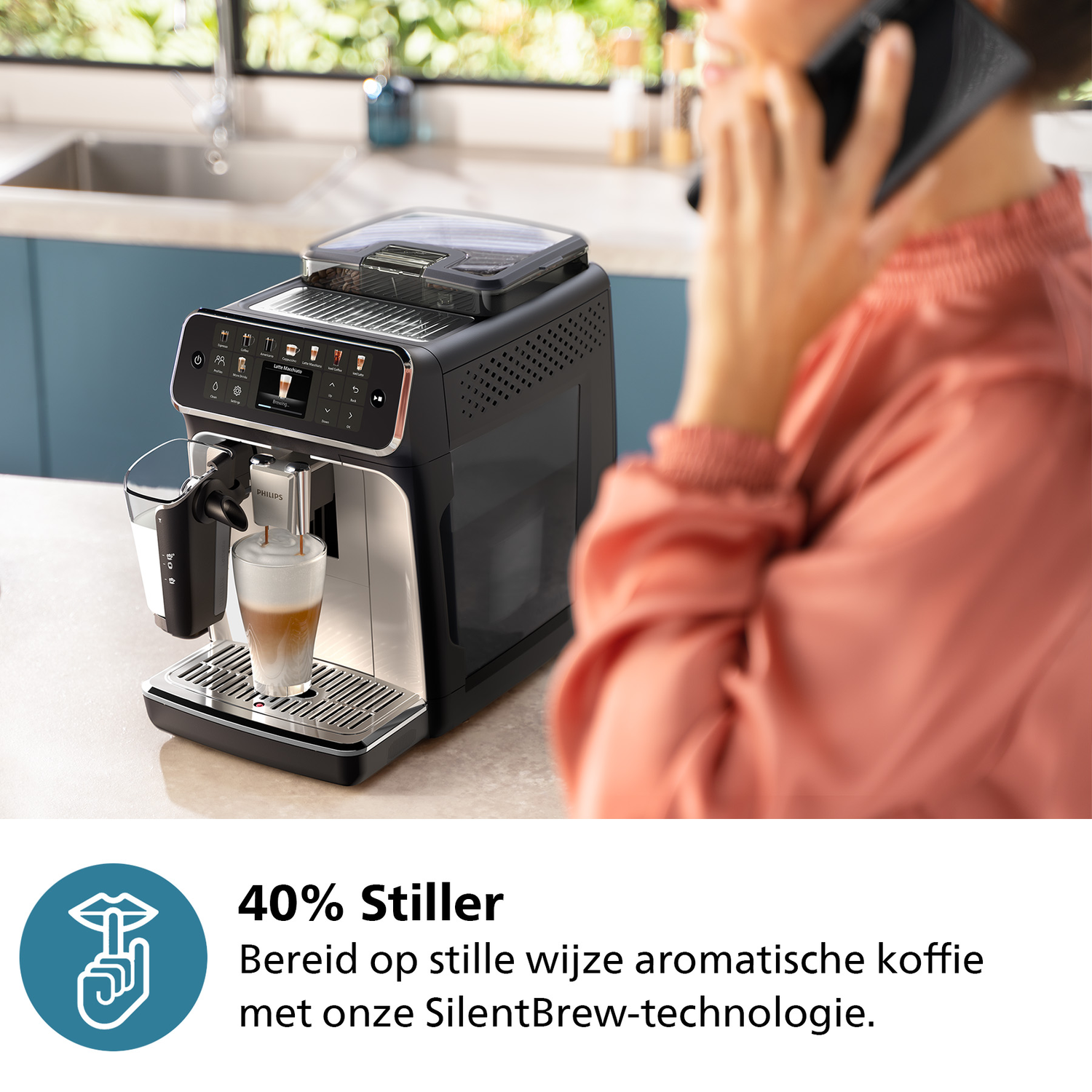 A woman on the phone beside a coffee machine, which is dispensing coffee into a glass.