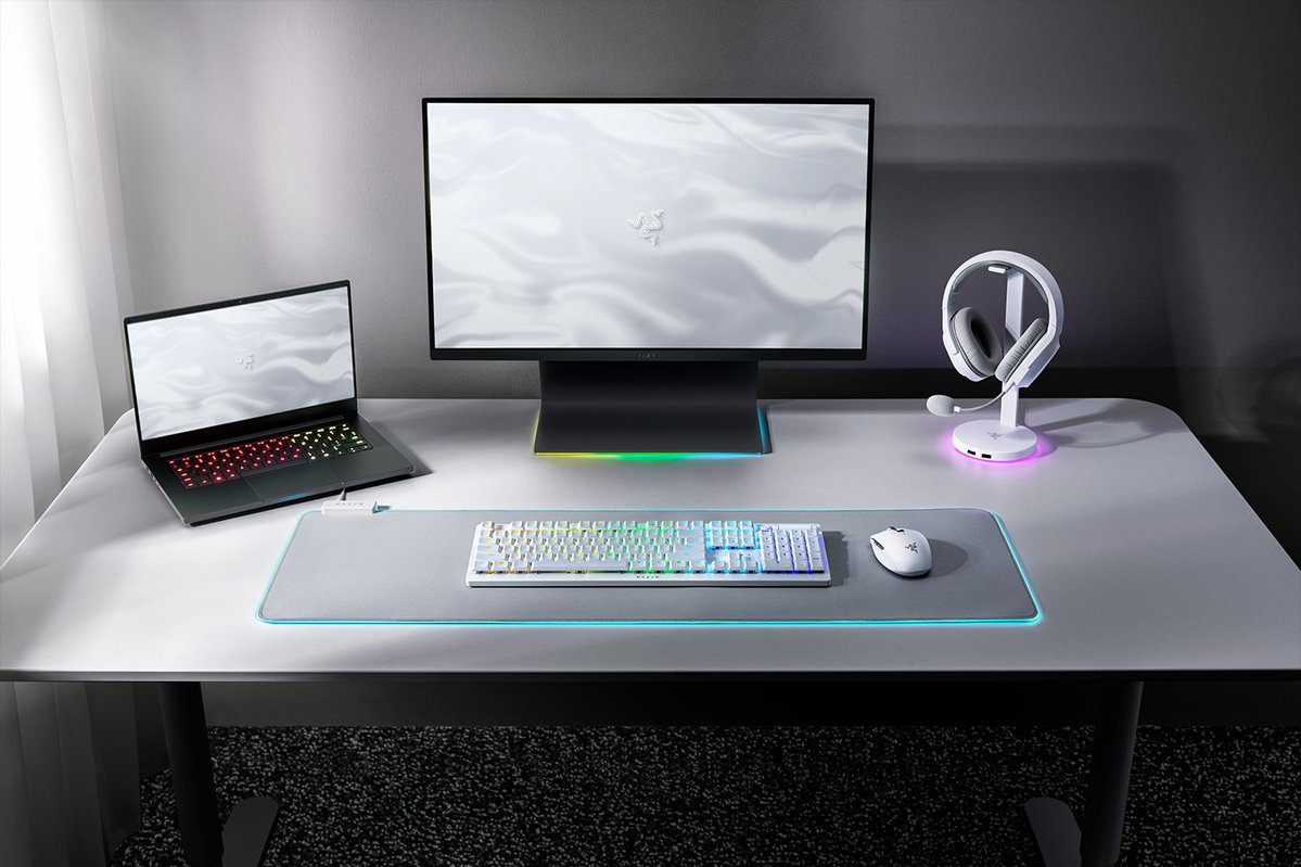 Konfiguracja do gier na białym biurku: laptop, monitor, klawiatura, mysz, zestaw słuchawkowy i podkładka pod mysz ze światłami LED.