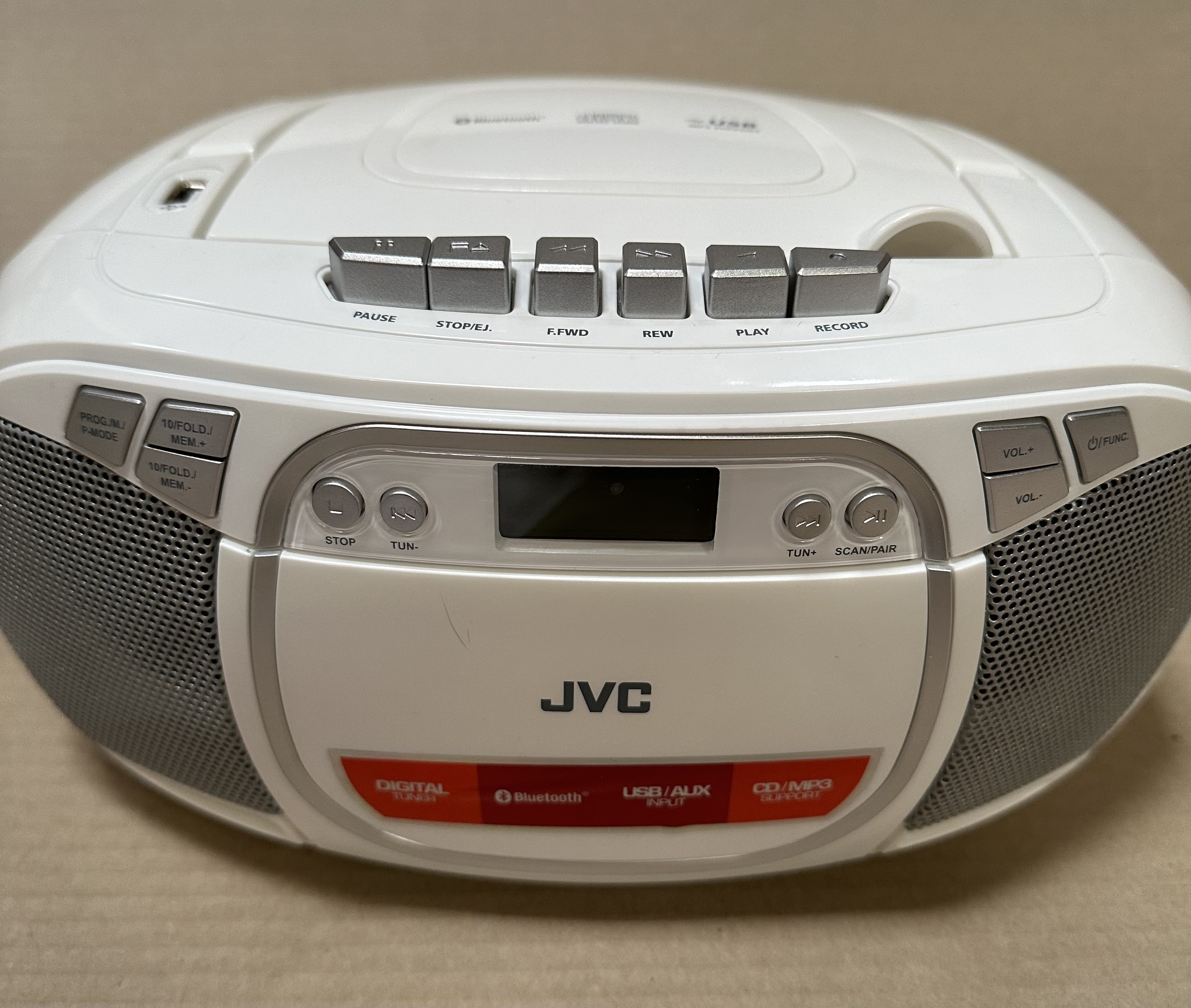 Biały odtwarzacz CD/MP3 JVC. Posiada przyciski do różnych funkcji, w tym pauzy, odtwarzania i nagrywania.