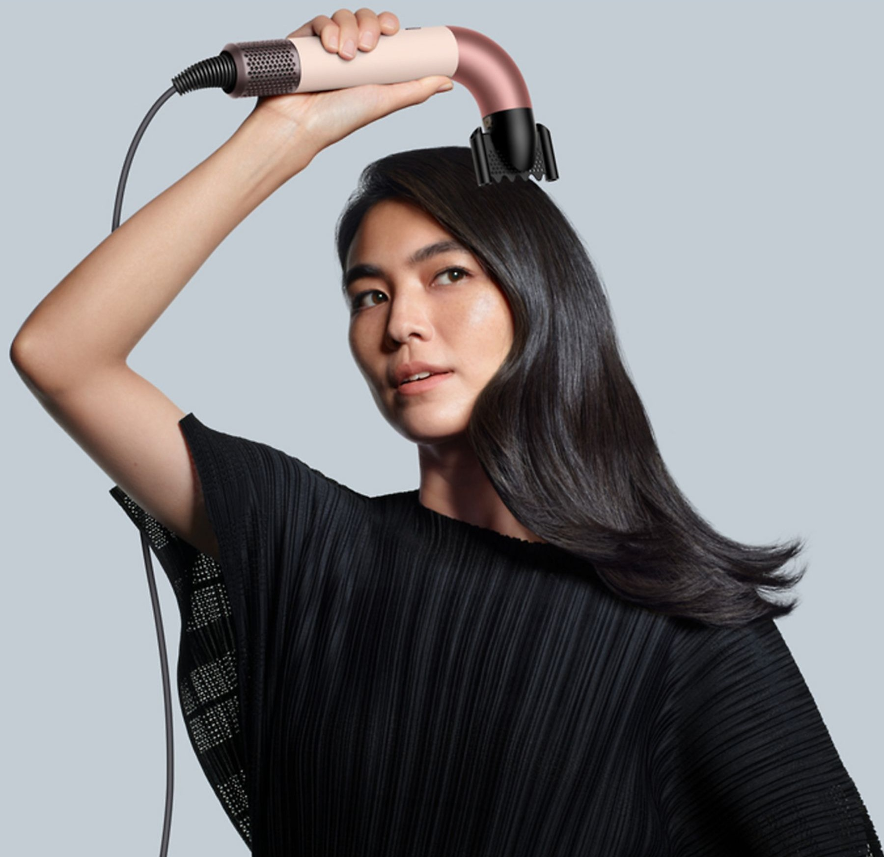 Kobieta trzymająca narzędzie do stylizacji włosów. Czarna koszula, szare tło.