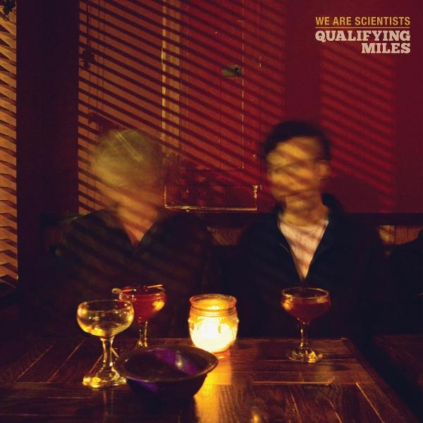 Schwach beleuchtete Barszene mit zwei verschwommenen Figuren, Getränken und einer Kerze. Rote Wände und Schatten von Jalousien.