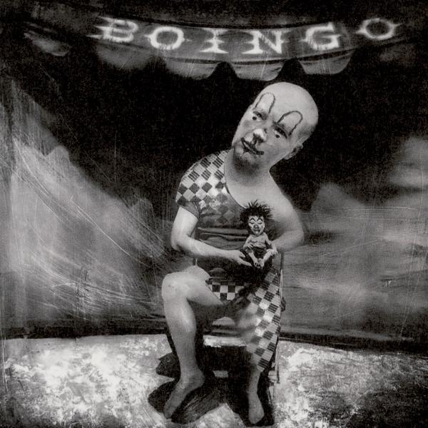 Ein Schwarz-Weiß-Foto eines Clowns, der eine kleine Puppe hält. Der Hintergrund ist dunkel und theatralisch.