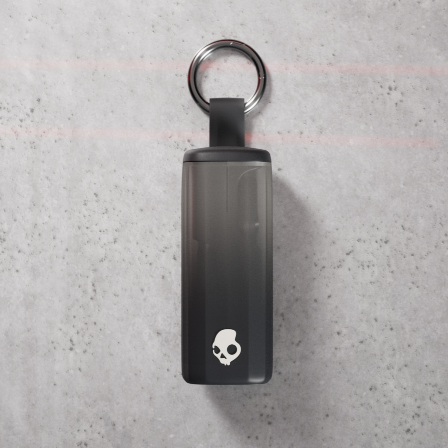 Ein schwarzer und grauer Skullcandy-Schlüsselanhänger mit silbernem Ring auf strukturiertem, grauem Hintergrund.