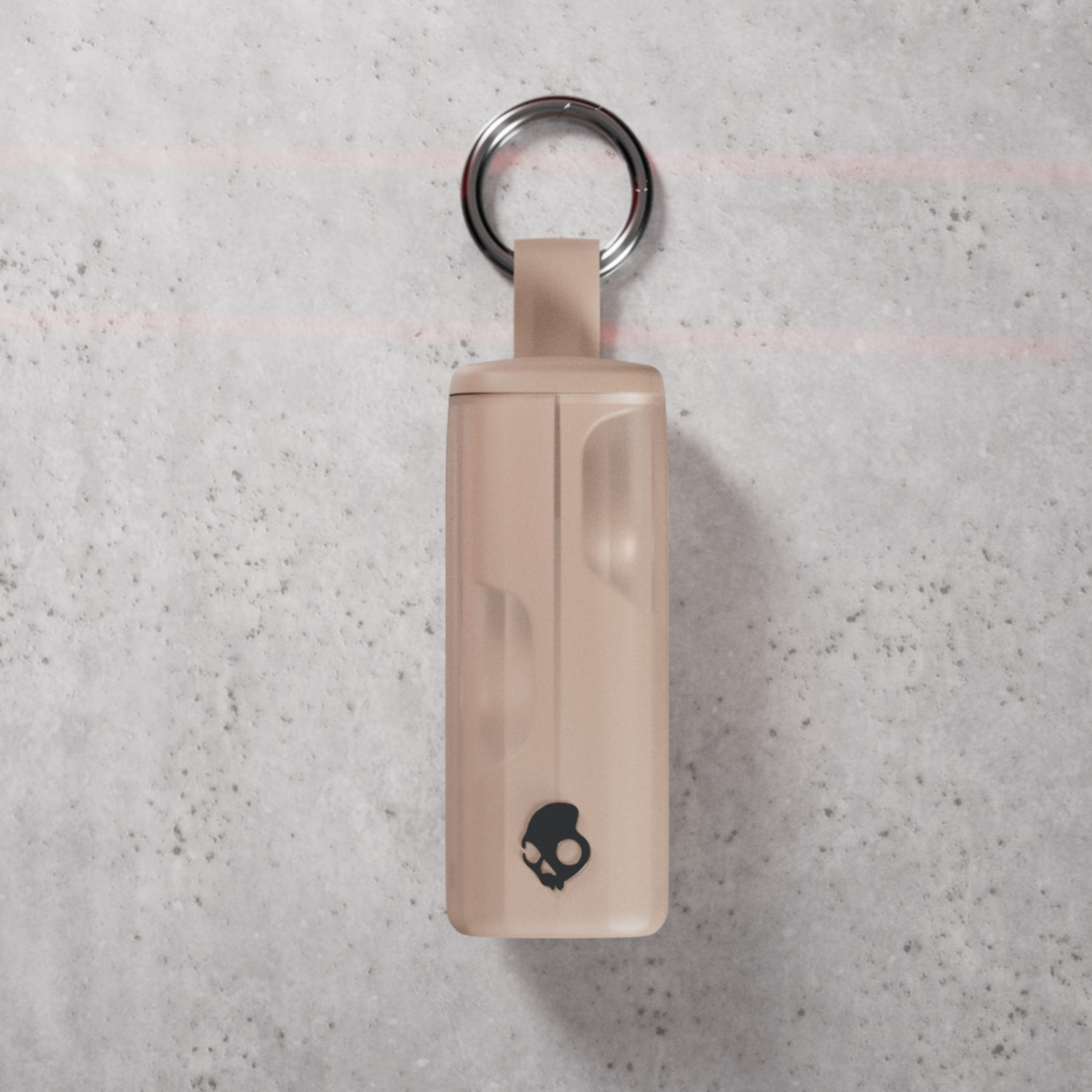 A small, beige keychain with a skull logo hanging from a silver ring, set against a textured gray surface.