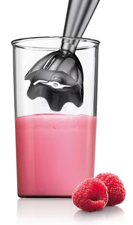 Blender w szklance z różowym płynem, maliny z przodu. Srebrny blender jest wewnątrz szklanki.