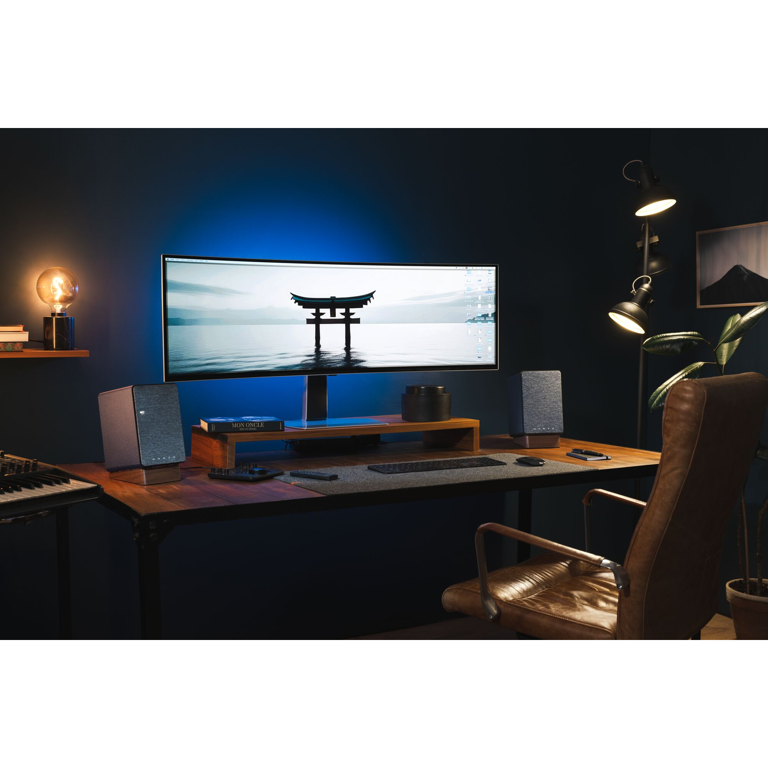 Bureau met een monitor, luidsprekers en decoraties. Donkere kamer met een lamp aan de muur.