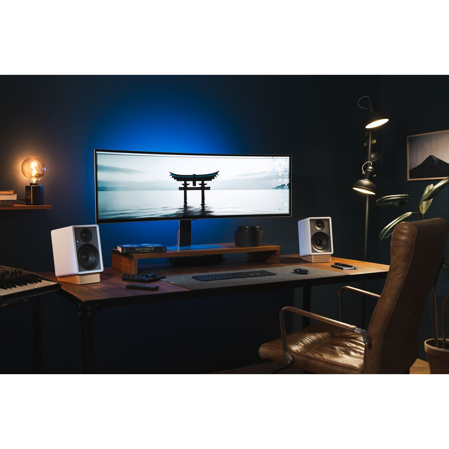 Een bureau-opstelling met een monitor, luidsprekers, toetsenbord en een lamp. Blauw licht verlicht de muur.