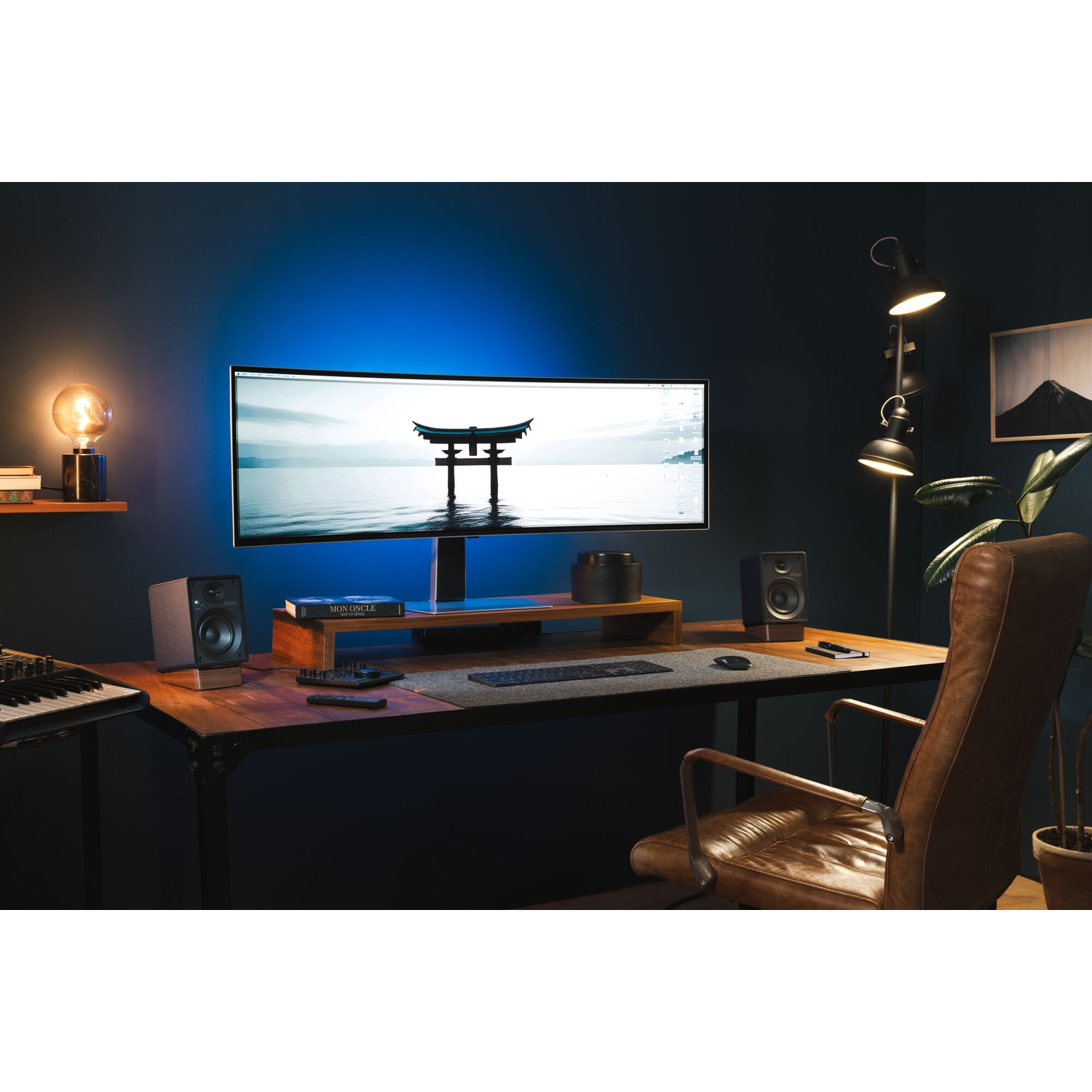 Bureau-opstelling met monitor, luidsprekers, toetsenbord en lamp. Het blauwe licht verlicht de muur.