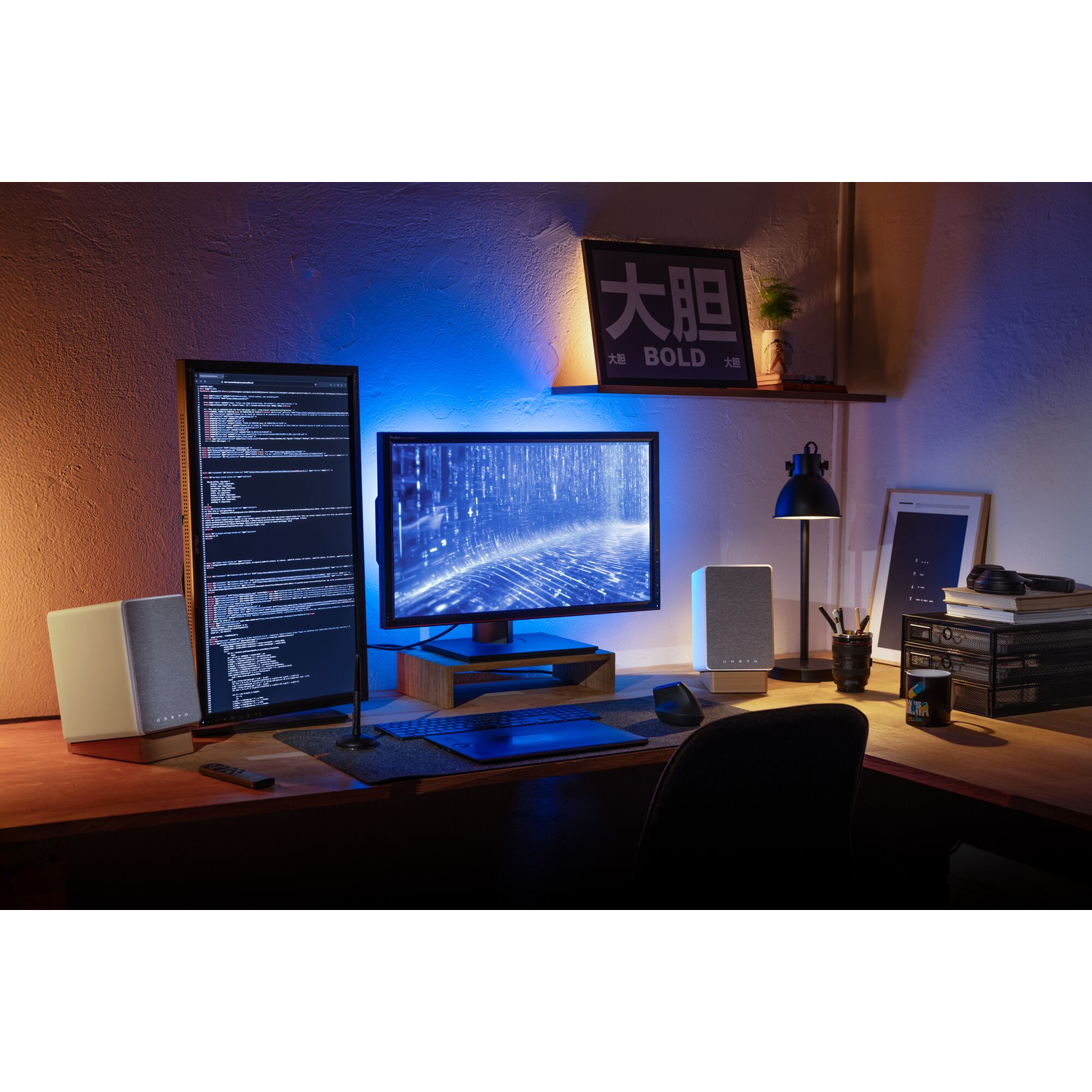 Een bureau-opstelling met monitoren, luidsprekers, toetsenbord en een lamp. Er staat een bord en een mok op het bureau.
