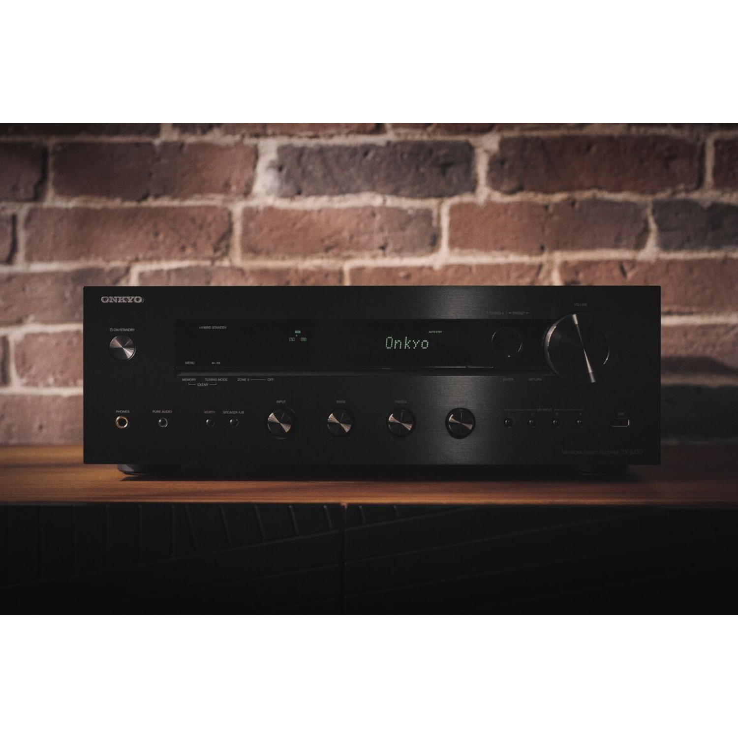 Black Onkyo audio receiver on a wooden surface. A brick wall forms the background.
