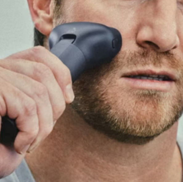 Mężczyzna goli twarz golarką elektryczną. Zbliżenie na skórę i narzędzie do golenia.