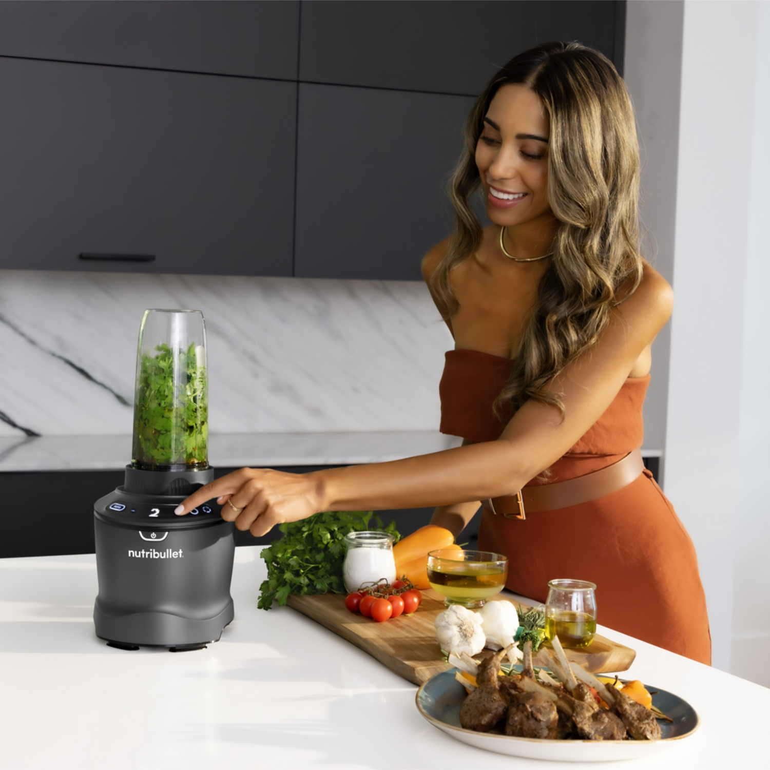 Mujer en la cocina usa una licuadora. Ingredientes: tomates, zanahorias y hierbas.
