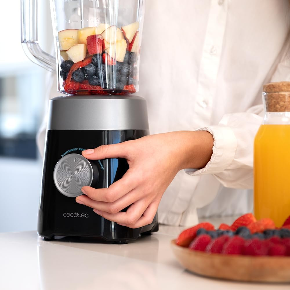 Una persona usando una licuadora con frutas dentro. Un tazón de frambuesas y jugo de naranja al lado.