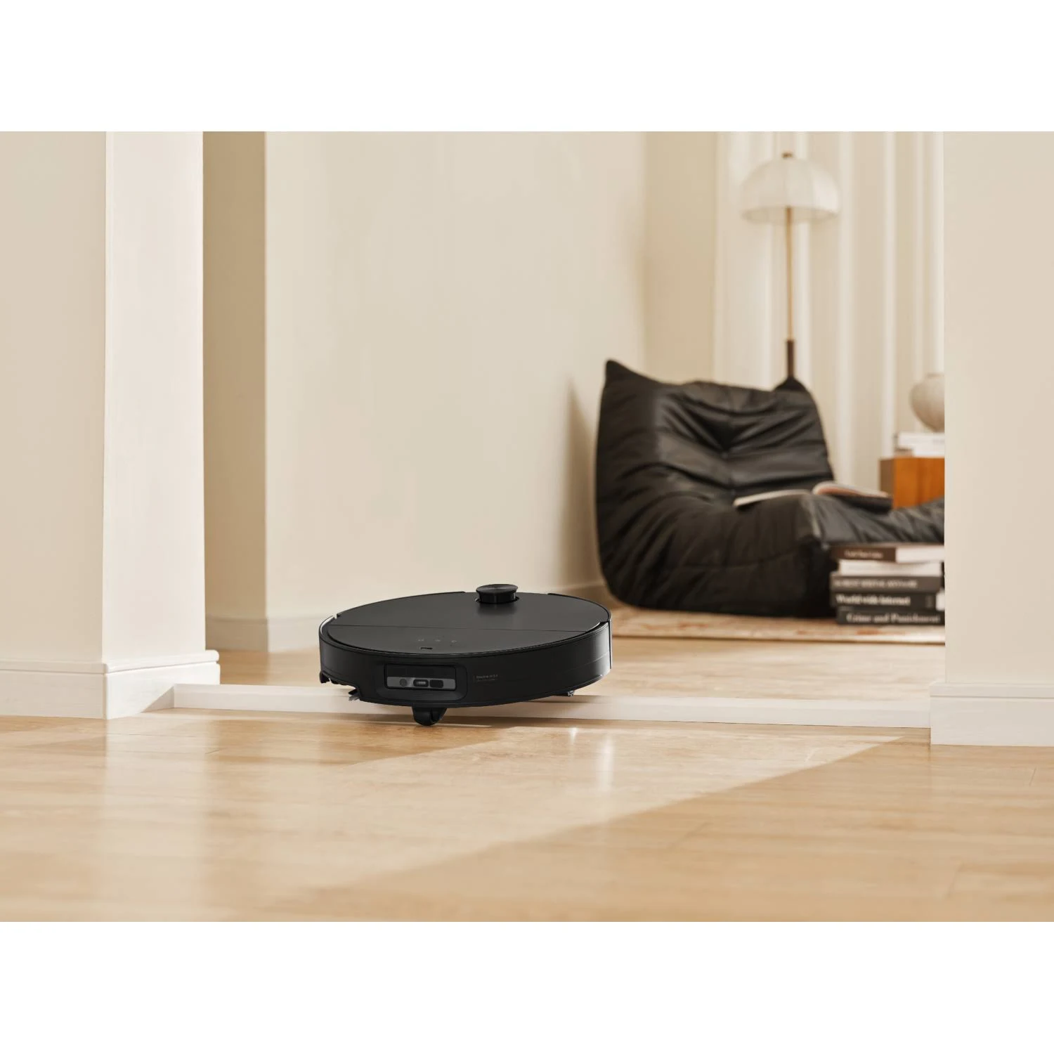 Aspiradora robot negra moviéndose en una habitación con suelo beige.