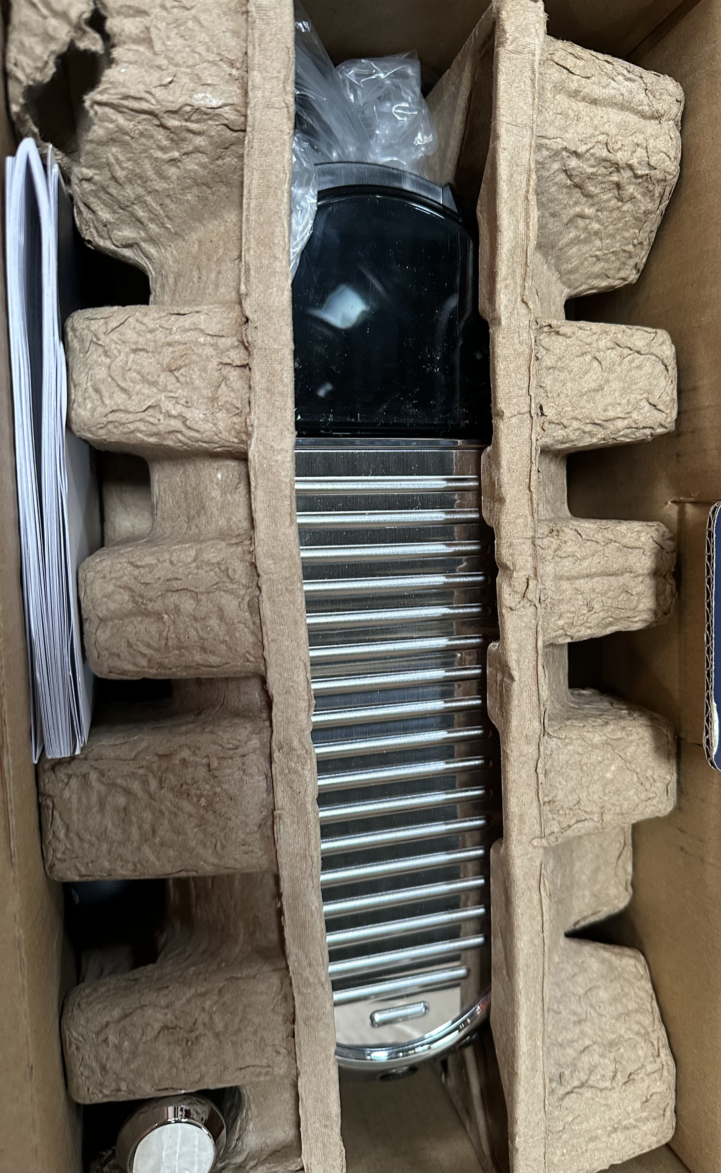 Zdemontowane urządzenie w kartonowym opakowaniu. Widoczne metalowe i czarne elementy.