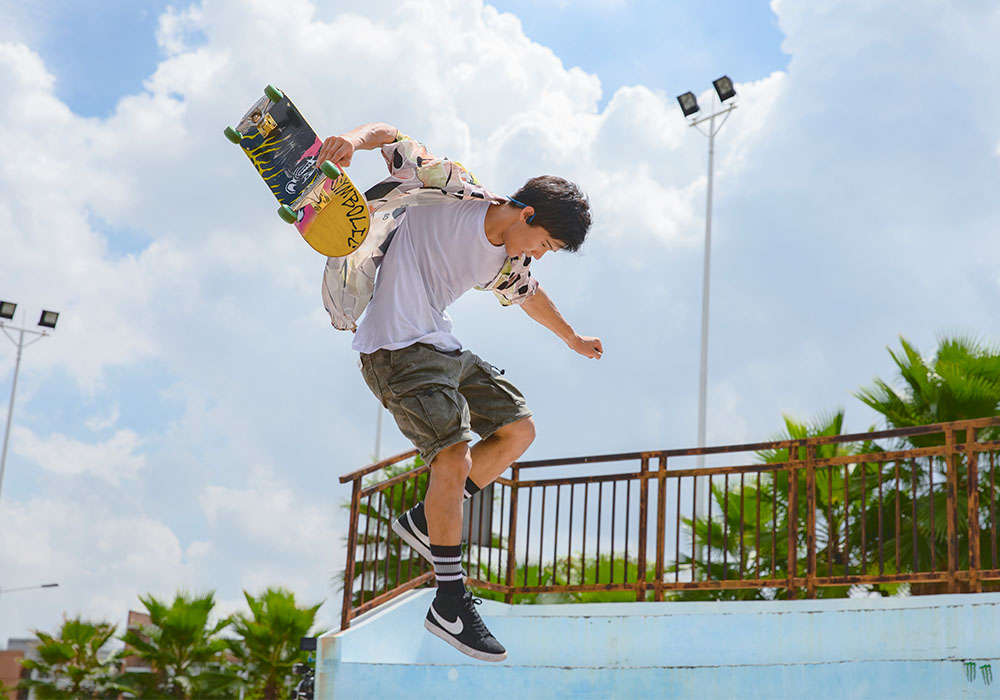 Młody mężczyzna skaczący ze deskorolką na tle niebieskiego nieba.