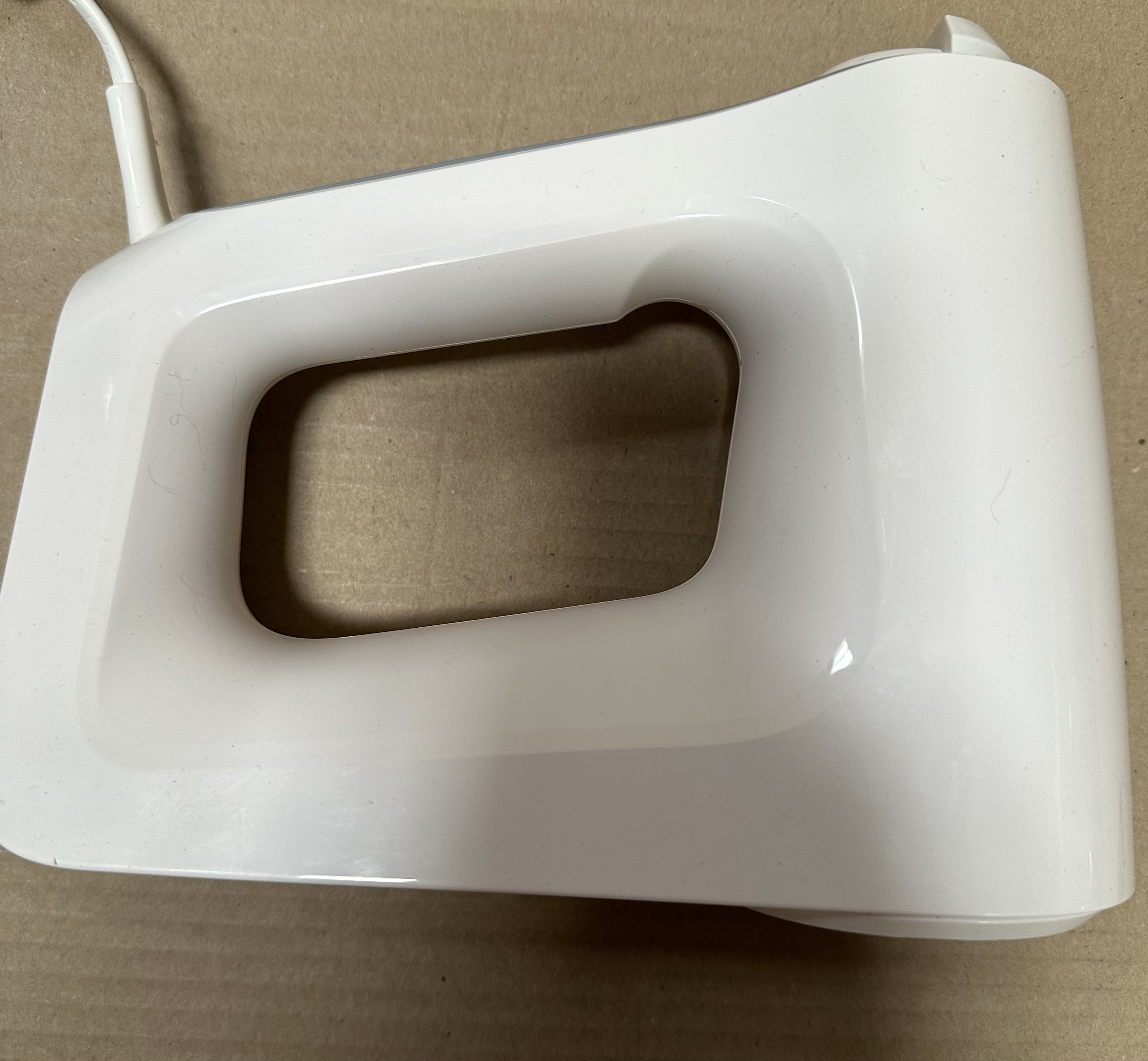 Biały mikser ręczny z uchwytem i kablem na brązowym tle.