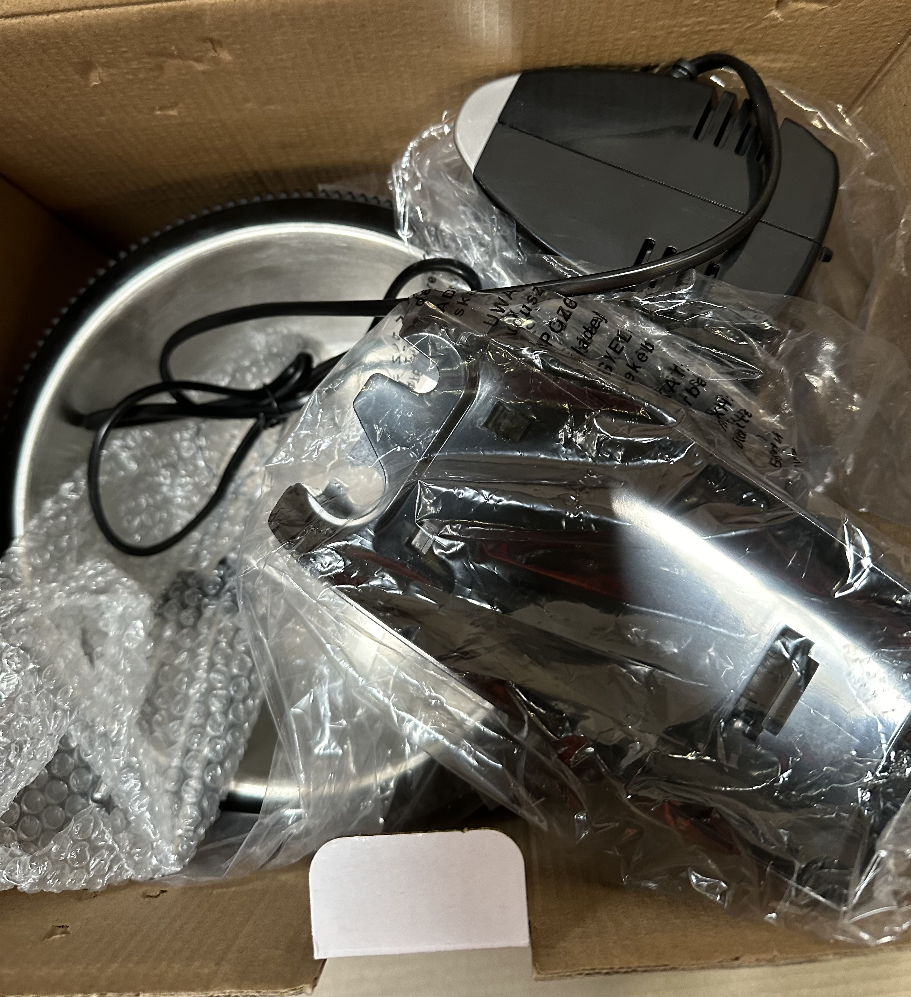 Młynek do kawy zdemontowany w pudełku. Części są owinięte folią. Widok z góry.