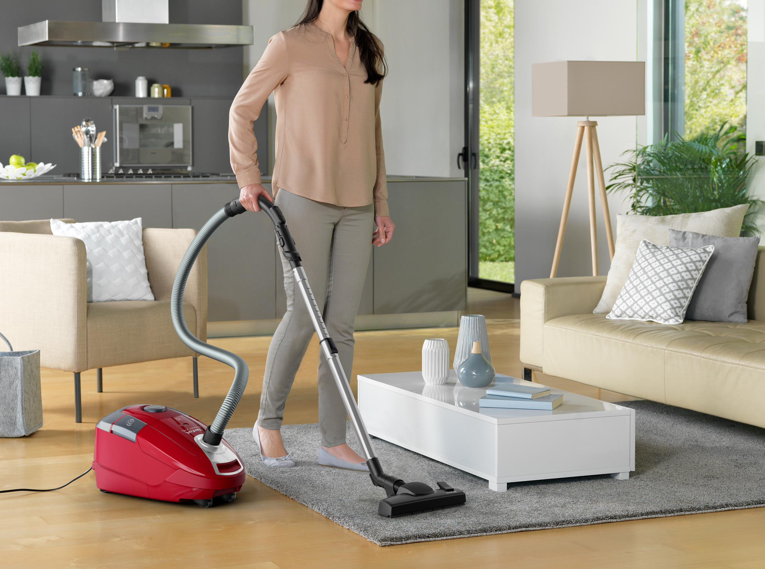 Eine Frau, die einen grauen Teppich mit einem roten Staubsauger in einem modernen Wohnzimmer saugt.